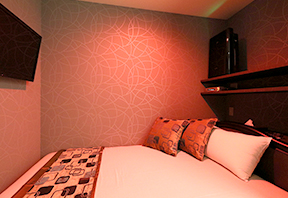 Bed with cushions and a wall-mounted TV in a softly lit room